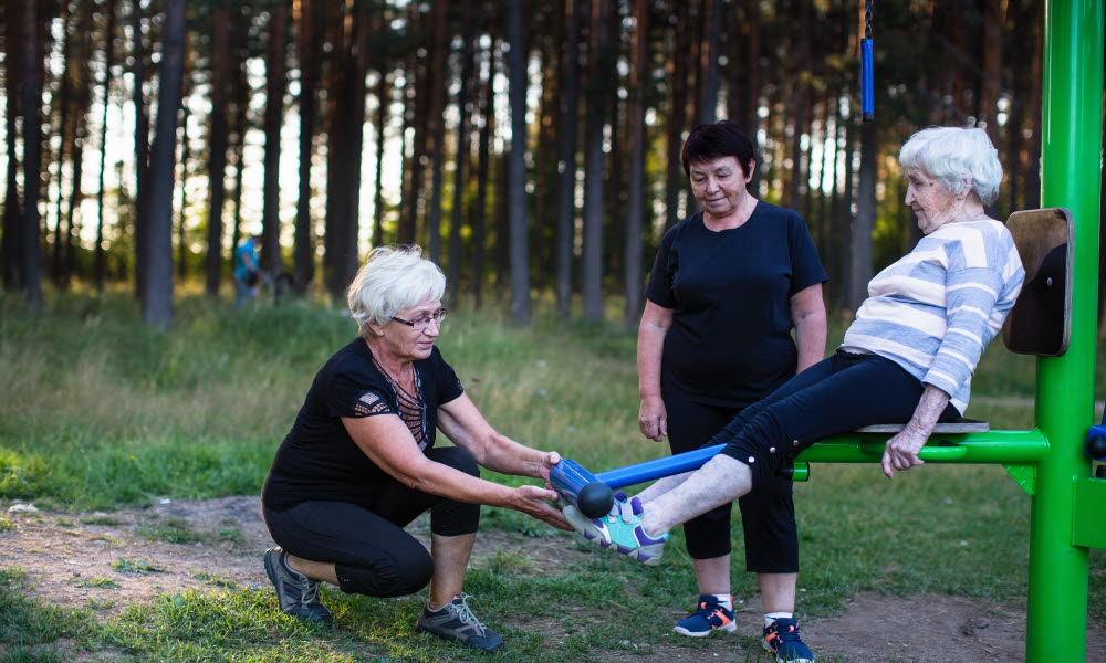 To eldre damer hjelper en tredje med utetrening